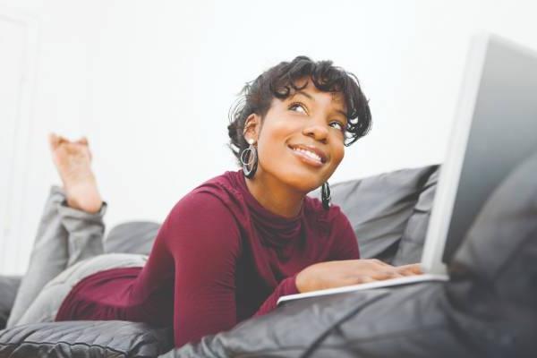 Woman laying on couch and smiling with laptop 