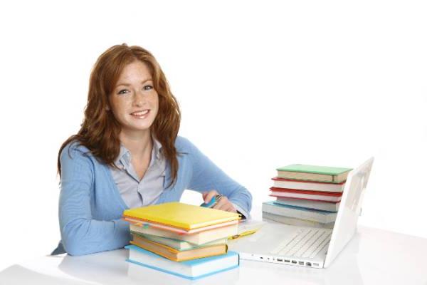 Female dual enrollment student sitting at a desk with her laptop and a stack of books.